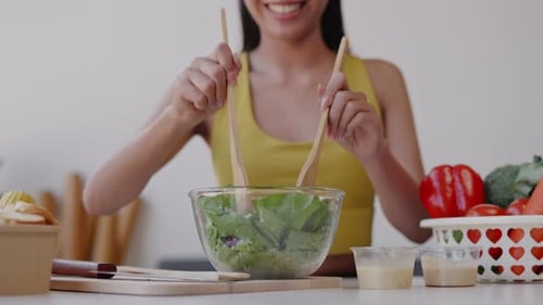 Young Woman Tossing Fresh Green Salad at Home