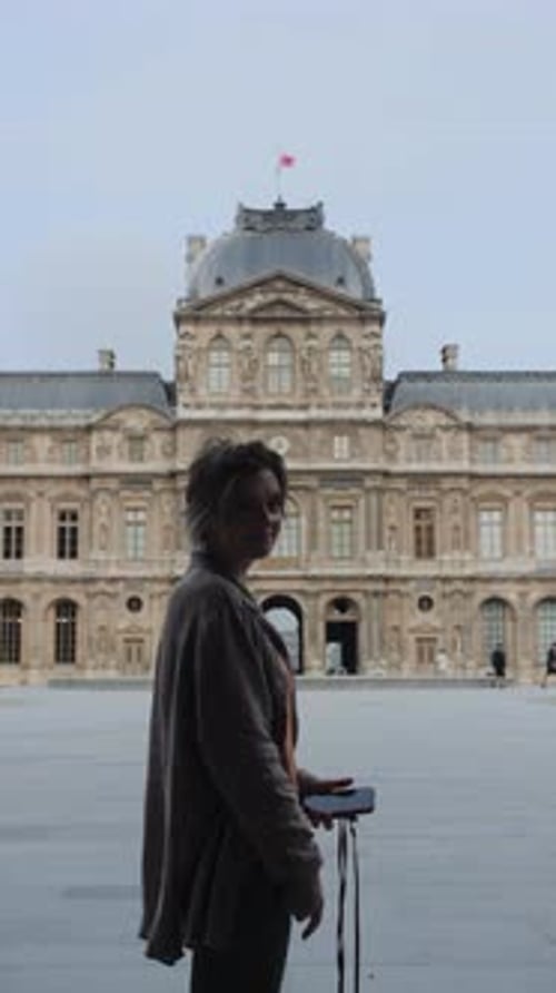 A woman stands in front of a large building, holding a cell phone