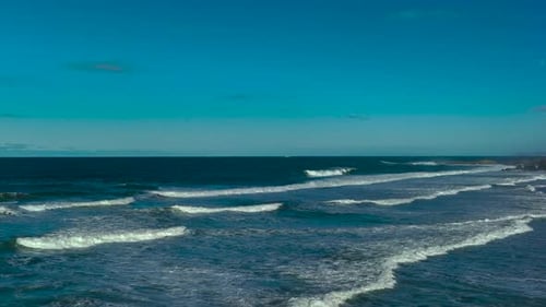 Flying From Beach To The Sea With Foamy Waves Under Blue Sky - Drone Shot