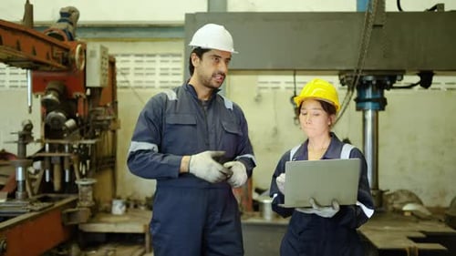 Professional asian engineers in overalls and hardhats walk through a heavy industry factory