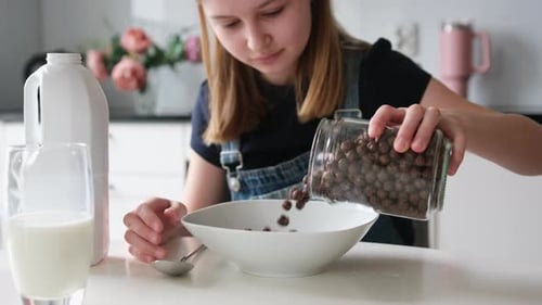 Girl Pours Cereal into Bowl at Table