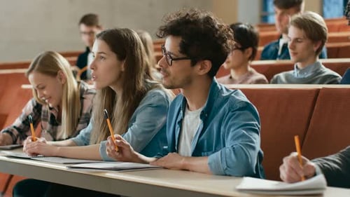 En el aula, estudiantes multiétnicos que escuchan a un profesor y escriben en cuadernos, todos
