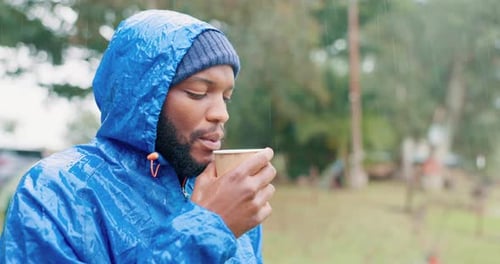 Man in Raincoat Drinks Cup Outdoors