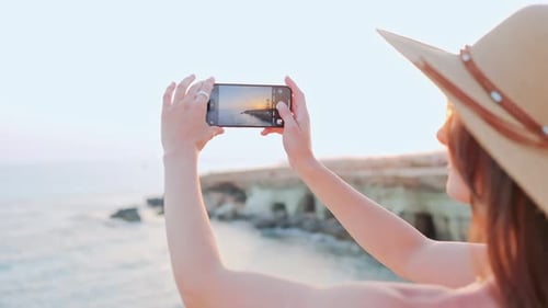 Overtheshoulder Closeup View of Young Happy Woman Taking Pictures of Picturesque Sunset Standing