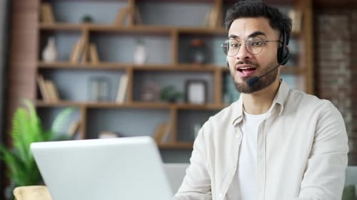 Confident businessman in headset talking on a video call using laptop sitting in home office