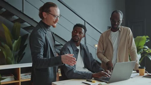 Team of Male Colleagues Discussing Business Plan On Laptop in Office