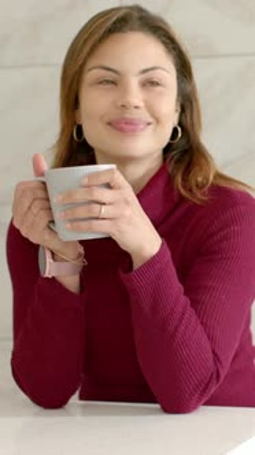 Vertical video: Lifting gray mug woman in maroon top at kitchen counter inhaling sipping reacting