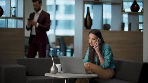 Confident businesswoman working laptop and answering phone call in modern office