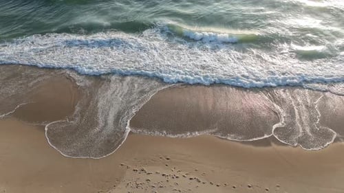 Luftaufnahme von sanften Wellen, die auf einen Sandstrand prasseln.
