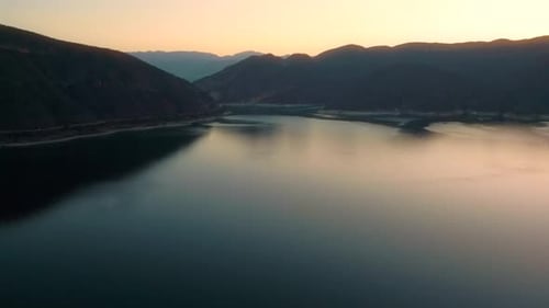 Aerial drone flying over a lake, water dam, with mountains at sunrise. Beautifull dreamy landscape
