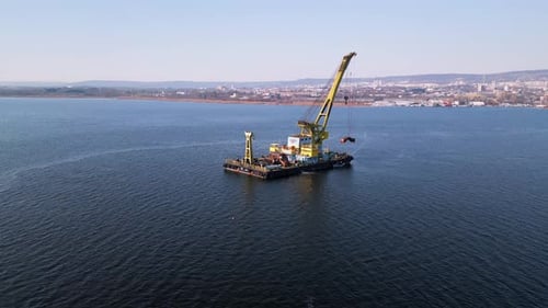 A Floating Crane Barge with a Large Yellow Crane Operates on Calm Waters Lifting an Object with Its