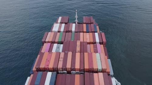 Aerial top view of a loaded container cargo vessel traveling over ocean.