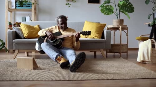 Man Sits on Floor Playing Guitar in Living Room
