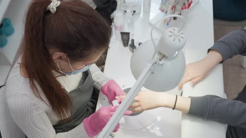 Top View of Nail Technician Filing Client Nails at Manicure Station with Tools