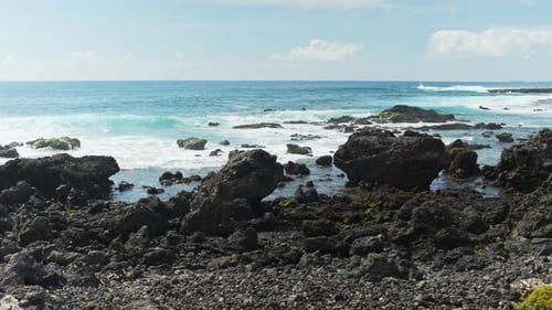 Panning shot at the sea over the black rocks at the seashore with splashing water, dynamic