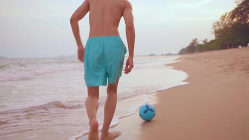 Asian young sportsman playing soccer alone on the beach during sunset.