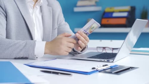 Adult Counts Money at Desk and Types on Laptop