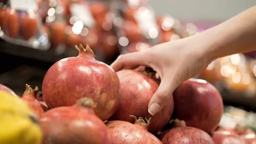 Young woman selects ripe pomegranates at the local farmers market closeup