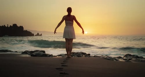 Woman in White Dress at Beach Enjoys Sunset in Sea and Raises Arms