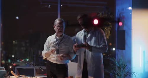 Adult Repairman Technician and Younger Lab Specialist Engineering in Dark Office Design Interior