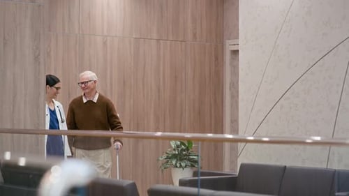 Medical Worker Assisting Senior Patient in Hall of Clinic