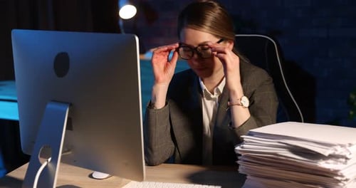 Workaholic. Overwhelmed woman taking off glasses and leaning on stack of documents near computer