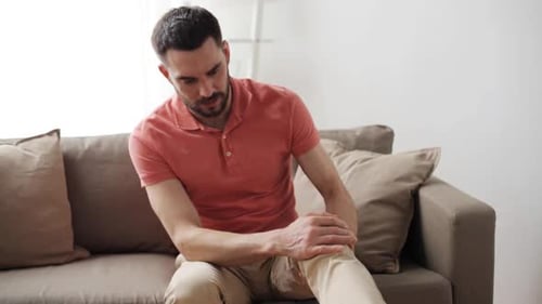 Man Sitting on Couch Massaging Sore Knee