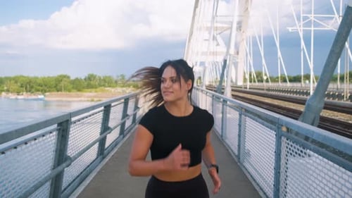 Young woman in black sport outfit running on city bridge.