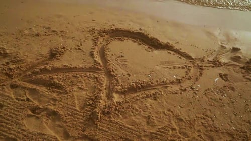 Heart shape love symbol drawn on golden sand beach with sea waves