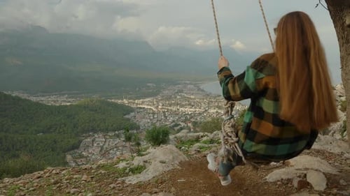 Experiencing extreme sensations, a young woman swings on swings at the edge of the cliff.