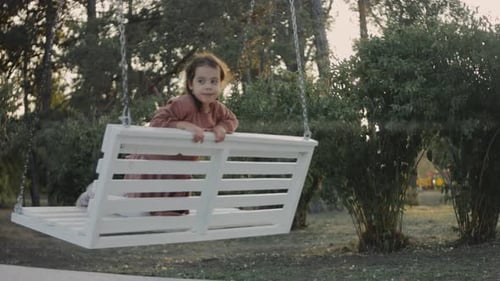 Little 5 Yo Girl Having Fun on a White Swing in a Quiet Treelined Park Background Preschooler