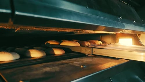 Ein Bäcker in der Fabrik stopft Brot zum Backen in den Ofen