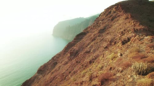Individual standing with arms outstretched on a cliff overlooking the ocean with hazy mountains in t