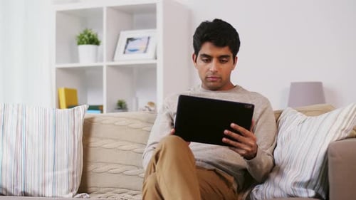 Man Sitting on Sofa Using Tablet at Home