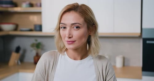 Woman looking at camera standing in the kitchen at home. Close up face attractive female housewife.