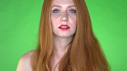 A close-up of a woman's face, showing neutral expression, on a seamless green studio background/gree