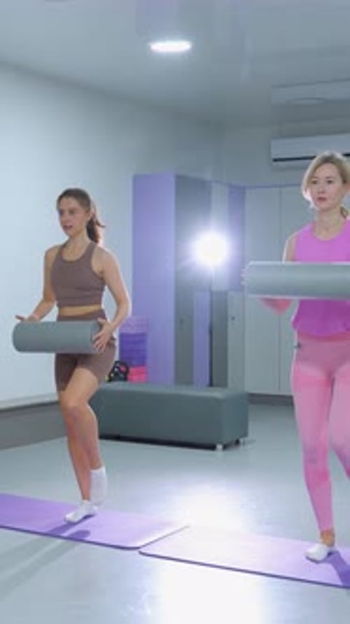 Two Women Balancing with Foam Rollers in Gym Workout Session