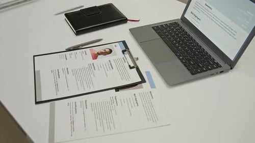 Office Desk with Applicants Resume on Laptop Screen, Notebook and Questionnaires