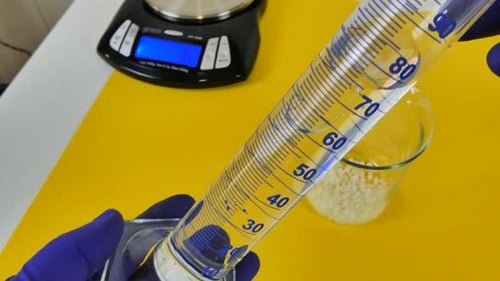 Laboratory technician pouring a transparent liquid from a measuring cylinder into a glass beaker