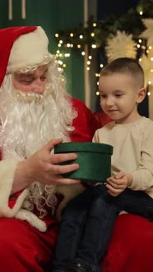 Papá Noel regala una caja de regalo verde a un niño pequeño en un ambiente festivo navideño