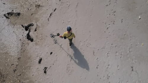 Aerial View of Man Using Metal Detector on Sandy Beach Searching for Treasure Among Footprints and