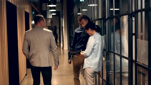 Two Smiling Diverse Businesspeople Talking Together in an Office Hallway with Colleagues