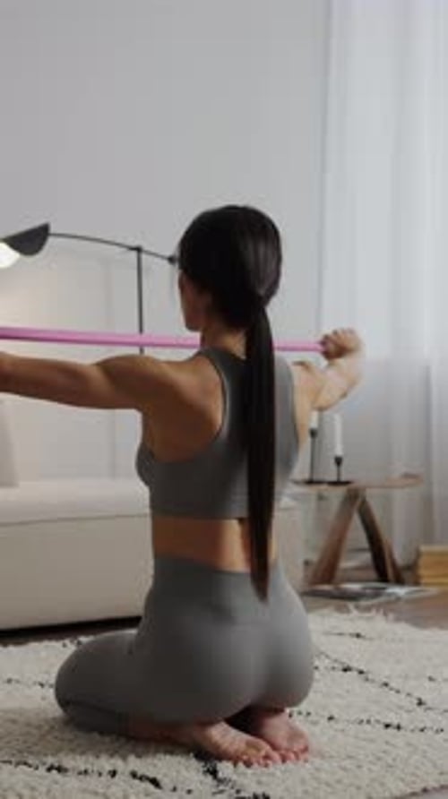 Focused Home Workout with Athletic Woman Kneeling on Carpet and Stretching Resistance Band Overhead