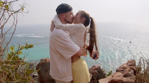 Romantic Kiss of Tourists on Cliff Edge with Turquoise Waves View