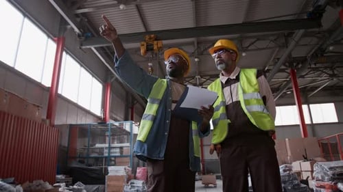 Two Diverse Warehouse Technicians with Clipboard Discussing Pallet Placement