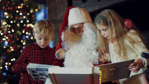 Niño y niña curiosos mirando un álbum junto a Santa Claus.