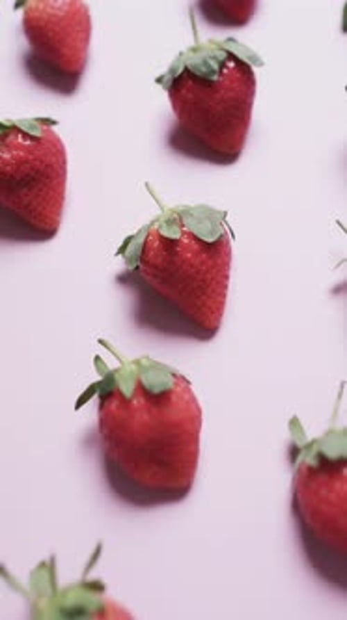 Vertical video of rows of strawberries with copy space on pink background