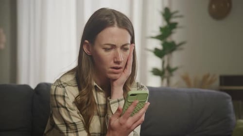 Concerned Woman Looking at Cell Phone on Sofa