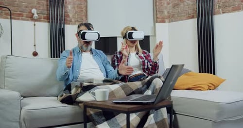 Couple Using VR Headsets on Sofa