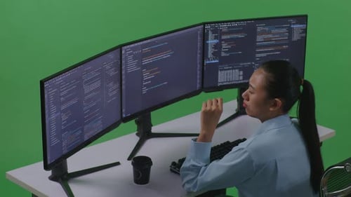 Side View Of Tired Asian Woman Yawning While Write Code With Multiple Computer In Green Screen